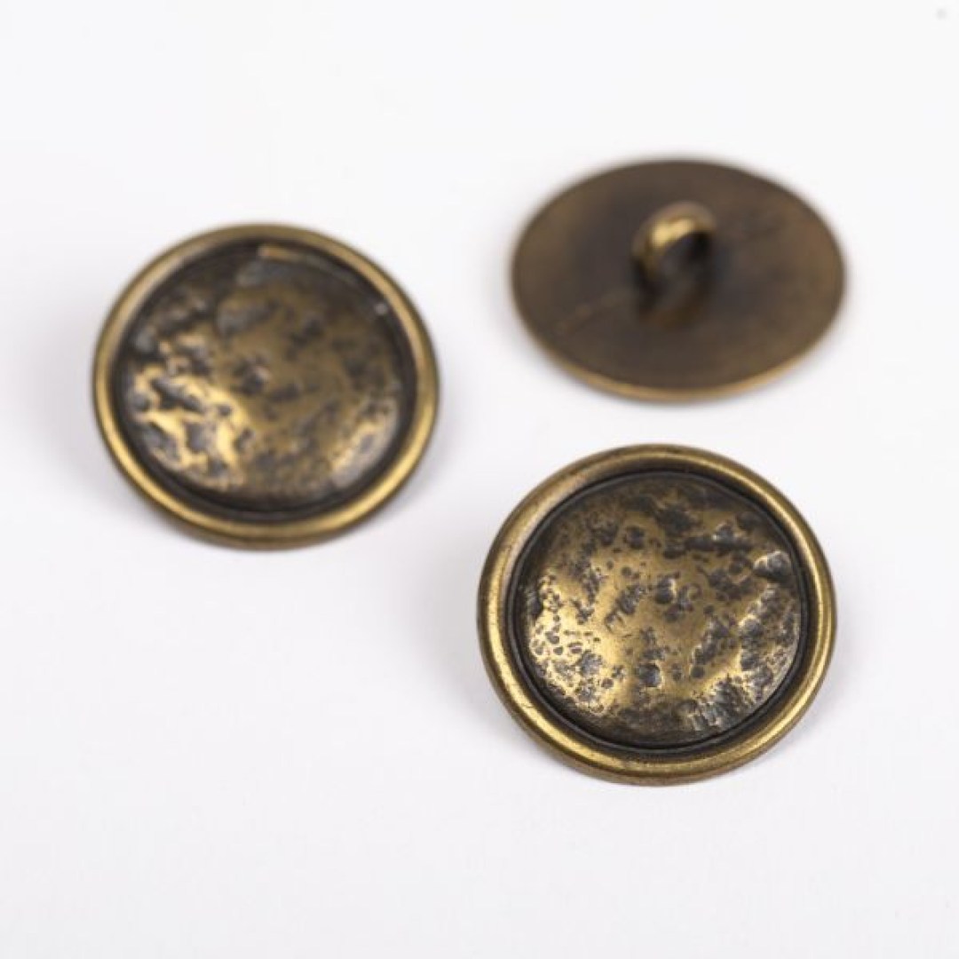 Μεταλλικό κουμπί DROPS Loop Brass 20 mm με ποδαράκι, σε απόχρωση χαλκού. Ανθεκτικό και κομψό, ιδανικό για ζακέτες, παλτό και πλεκτά projects.